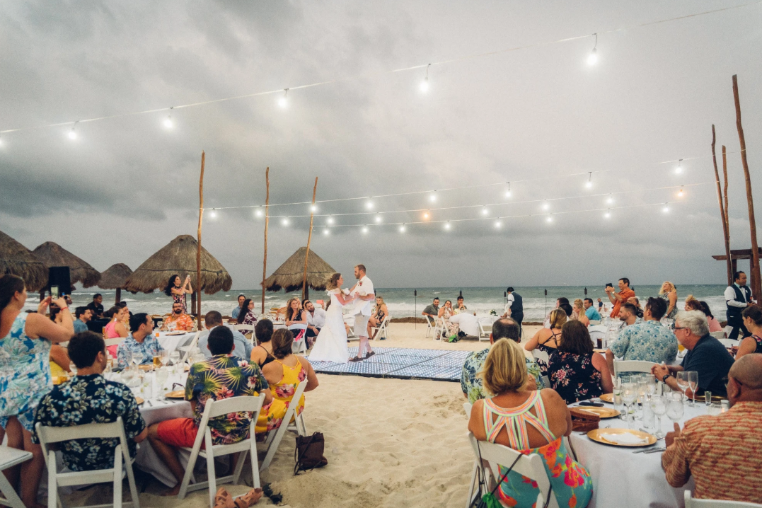 Couple sharing their first dance on a beach dance floor under string lights